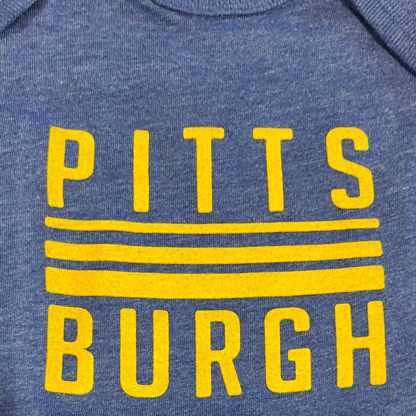 Blue baby onesie with 'Pittsburgh' printed in yellow on a textured surface